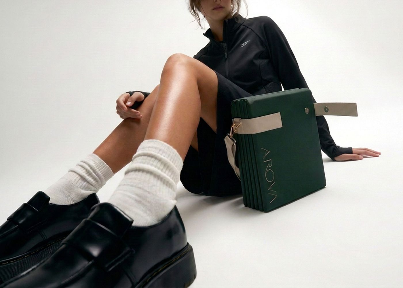 A woman in loafers sitting beside the folded AROVA mat