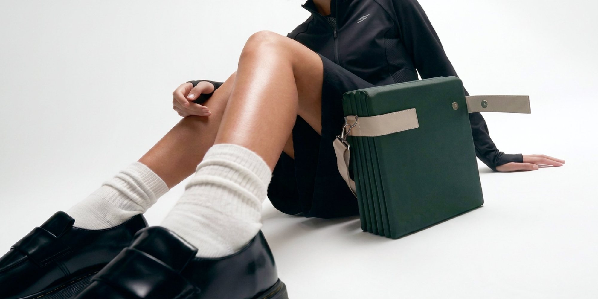 A woman in loafers sitting on the floor beside the folded AROVA mat