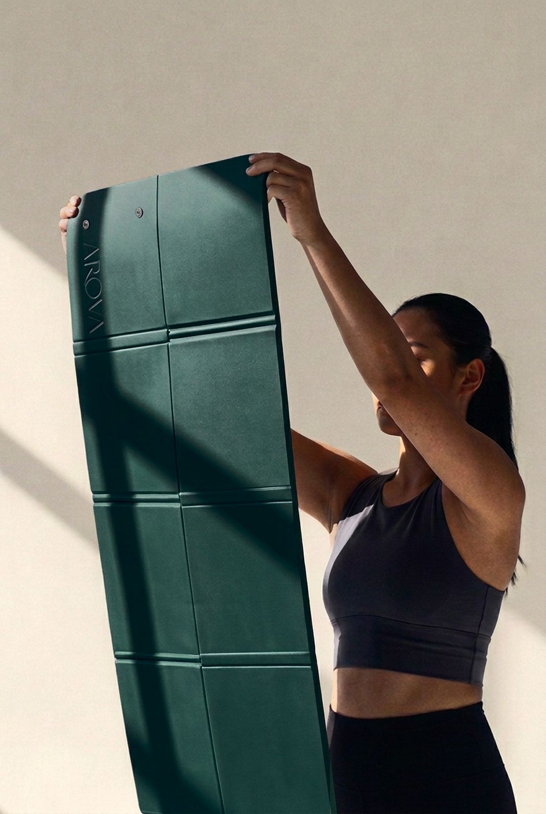 A woman holding up the unfolded AROVA mat, its even panels running the full length